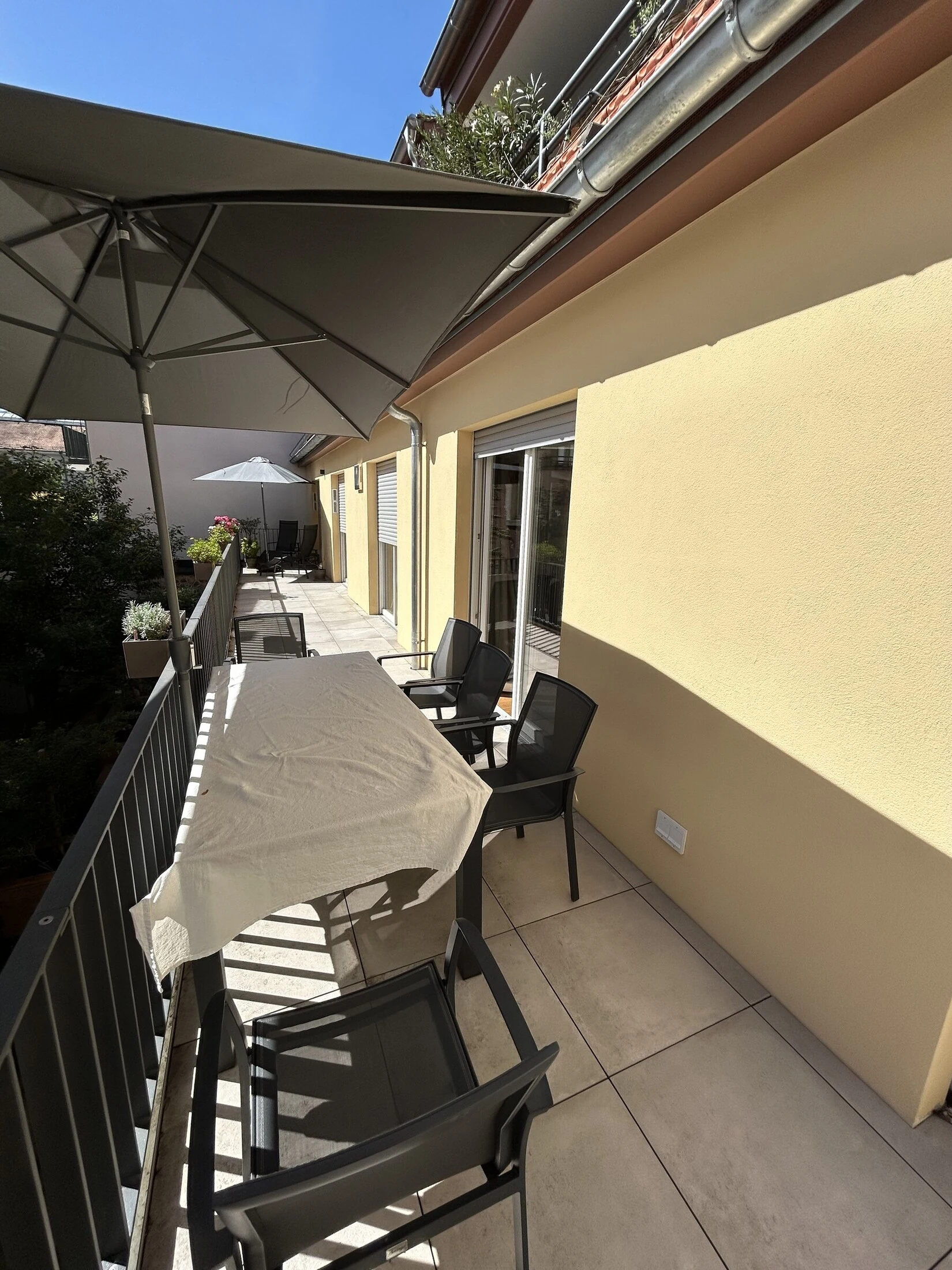 Long south-facing terrace with an outdoor dining table, chairs and a parasol